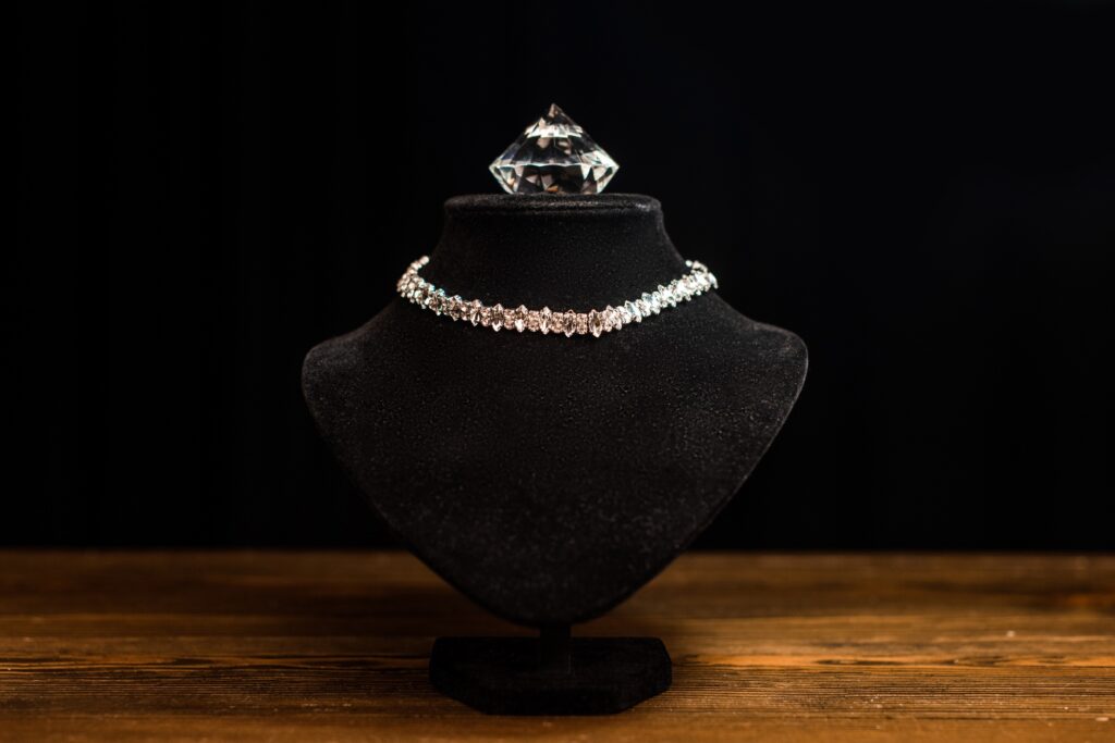 Necklace stand with necklace and diamond on wooden table isolated on black